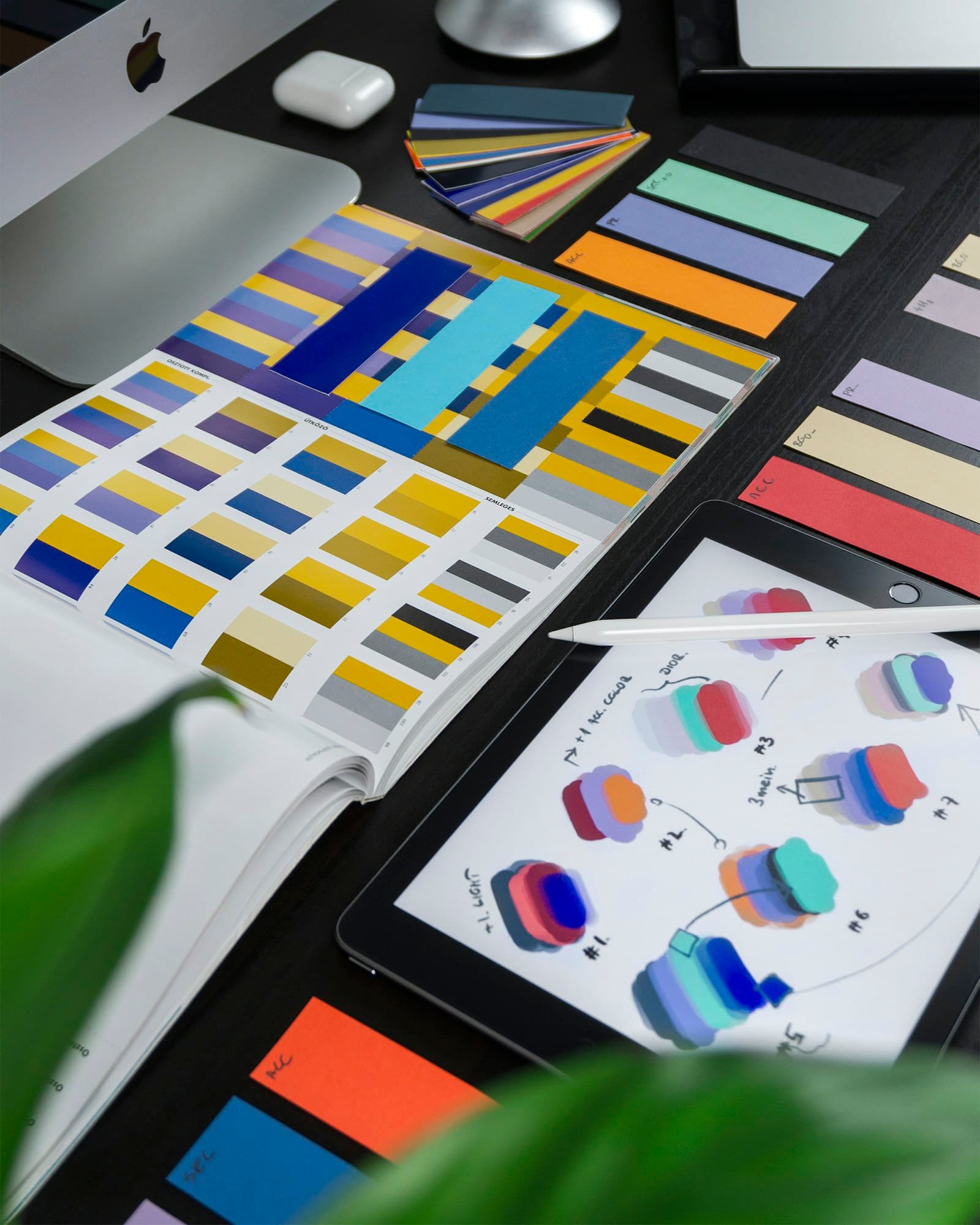 A designer's desk with printed colour palettes and logo sketches on a tablet