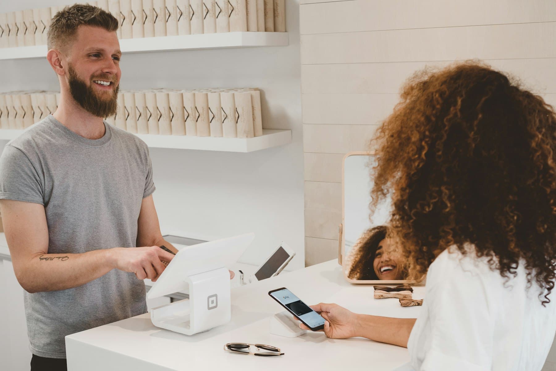 A shop owner smiling with a customer at the counter of a small bright store