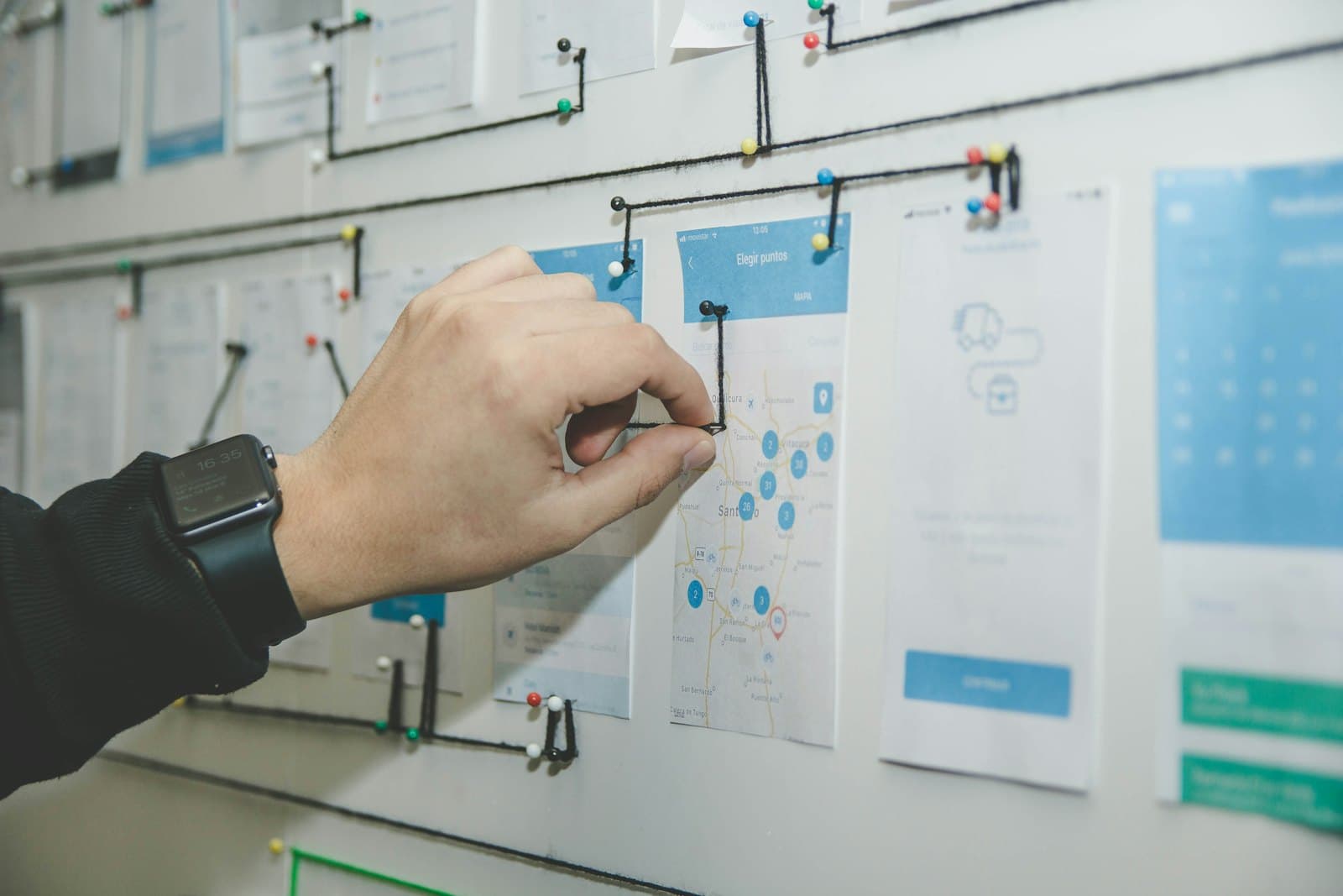 A hand pinning app screens to a planning wall connected by threads